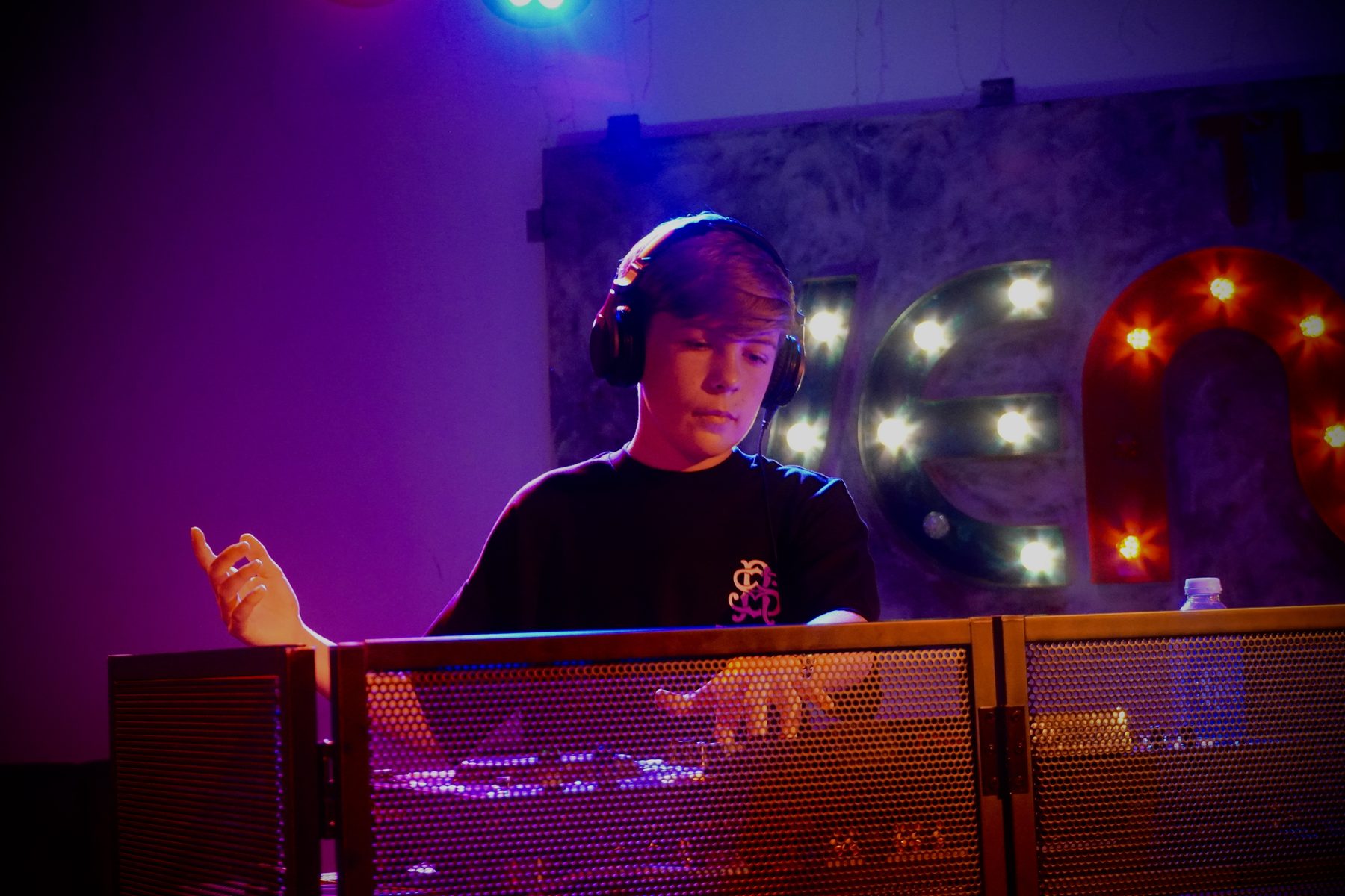 Oliver Newton DJing on stage with his hand raised, lit in purple and pink