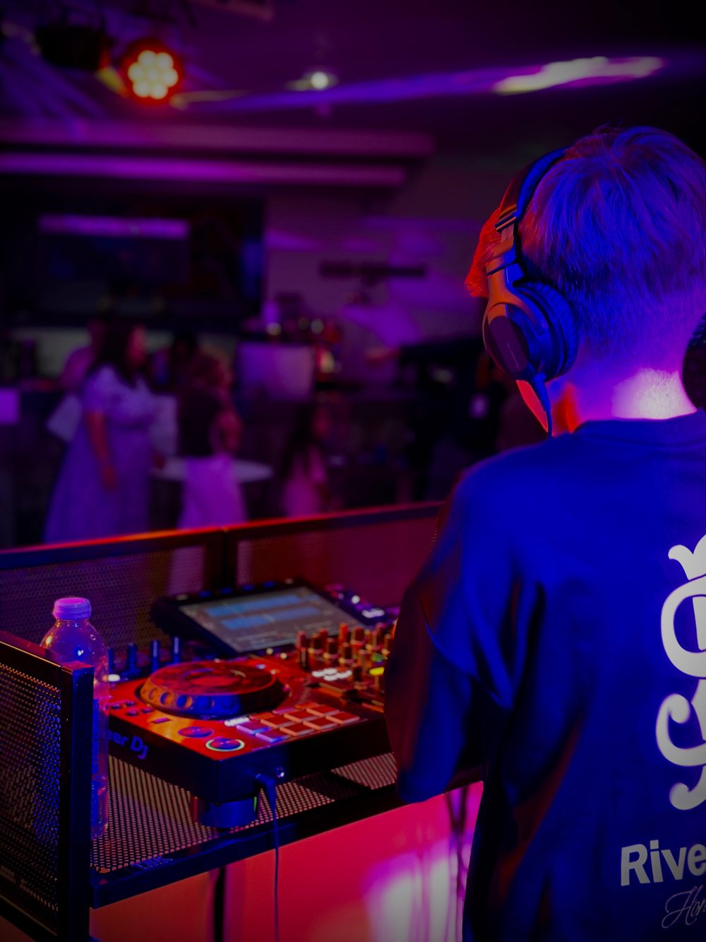 Oliver Newton at the decks in headphones, looking out over the dance floor